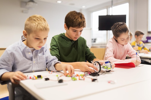 education, children, technology, science and people concept - group of happy kids building robots at robotics school lesson