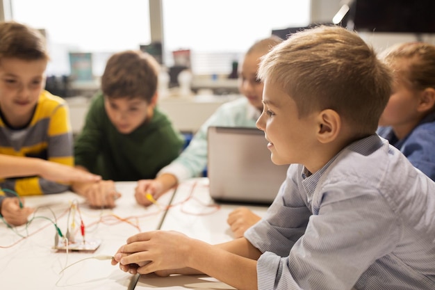 education, children, technology, science and people concept - group of happy kids with laptop computer playing and invention kit at robotics school lesson