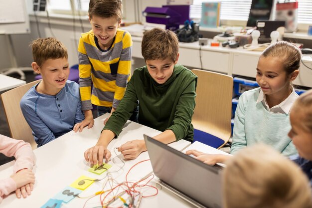 education, children, technology, science and people concept - group of happy kids with laptop computer playing with invention kit at robotics school lesson