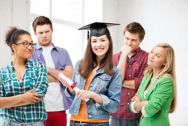 Foto concetto di educazione e competizione - ragazza con cappello di laurea con certificato e studenti