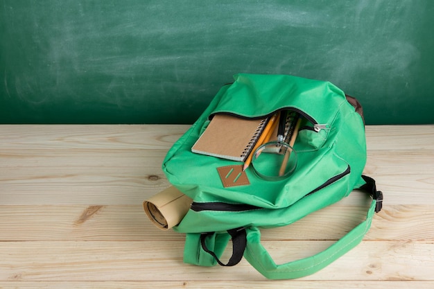 Photo education concept - green backpack, notebooks and school supplies on the background of the blackboard