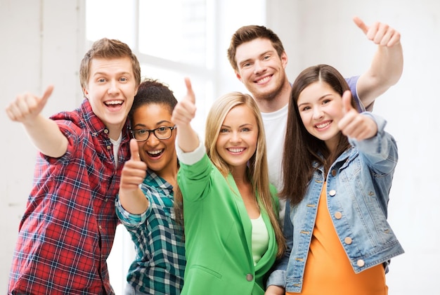 Foto concetto di educazione - felice squadra di studenti che mostra i pollici in su a scuola