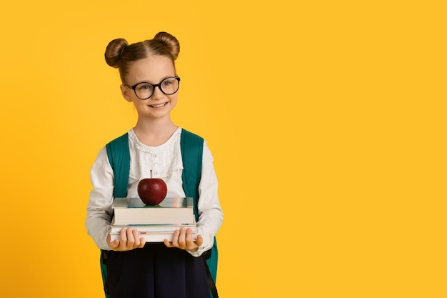 Education concept little cute schoolgirl holding stack of books and red apple