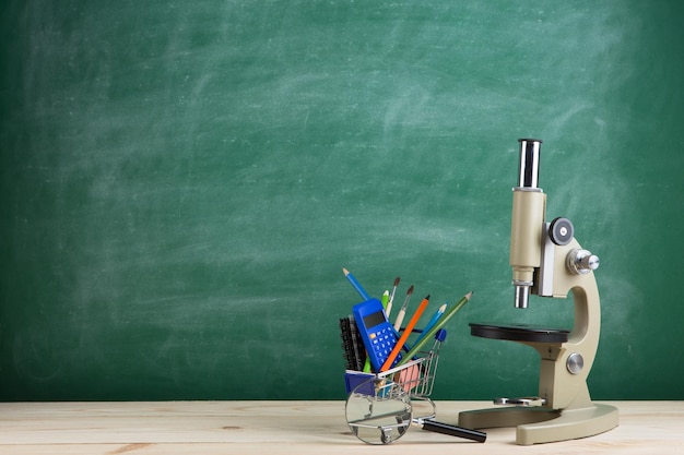 講堂の黒板の背景の机の上の教育概念顕微鏡
