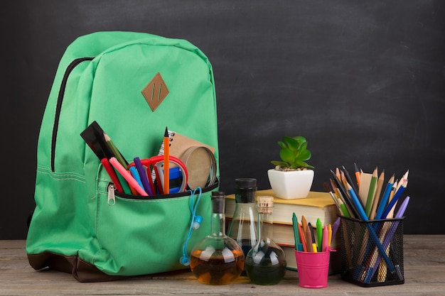 Education concept school backpack with books and other supplies blackboard background