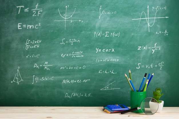 Education concept school supplies on the desk in the auditorium blackboard background