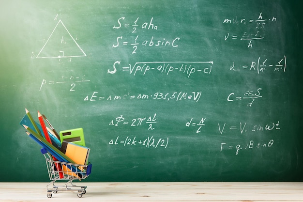 Education concept school supplies in a shopping cart on the desk in the auditorium blackboard background