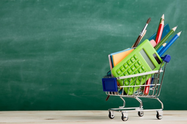 Education concept school supplies in a shopping cart on the desk in the auditorium blackboard background