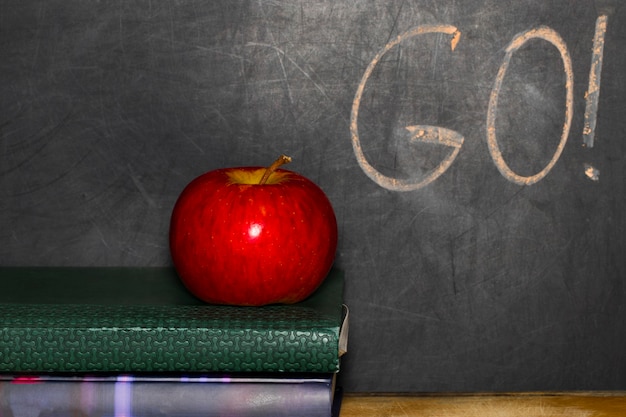 Education concept with apple on stack of books on blackboard background.