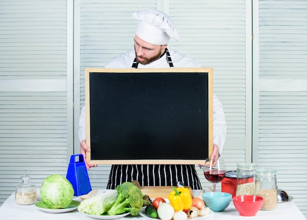 Education of cooking and food preparation Chief cook teaching master class in cooking school Master cook giving cooking class Man in chef hat holding empty blackboard copy space