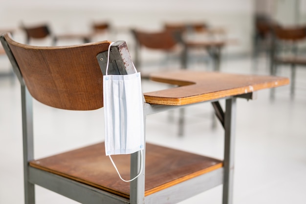 Education during COVID-19: A used medical facemask hangs on a wood lecture chair in empty classroom during COVID-19 pandemic