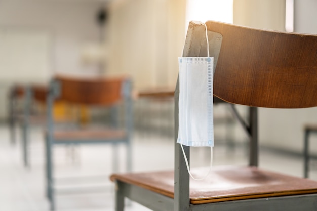 Education during COVID-19: A used medical facemask hangs on a wood lecture chair in empty classroom during COVID-19 pandemic