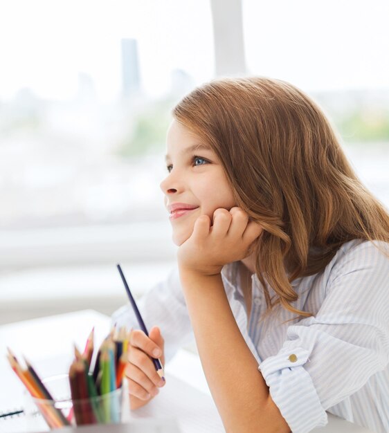 Photo education, creation and school concept - smiling little student girl drawing and daydreaming at school