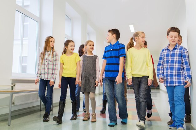 Concetto di istruzione, scuola elementare, bevande, bambini e persone - gruppo di scolari sorridenti che camminano nel corridoio