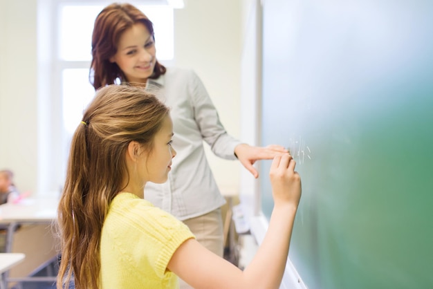 Istruzione, scuola elementare, apprendimento, matematica e concetto di persone - piccola studentessa sorridente che scrive numeri sulla lavagna verde in classe