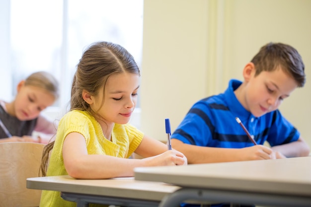 education, elementary school, learning and people concept - group of school kids with pens and notebooks writing test in classroom