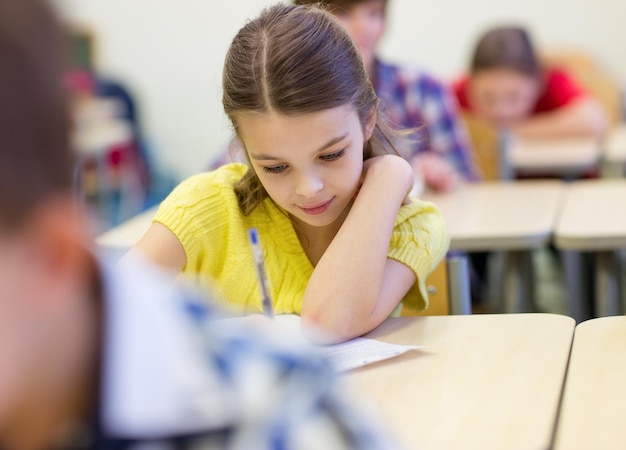 education, elementary school, learning and people concept - group of school kids with pens and notebooks writing test in classroom