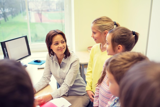 Education, elementary school, learning and people concept - group of school kids with teacher talking in classroom