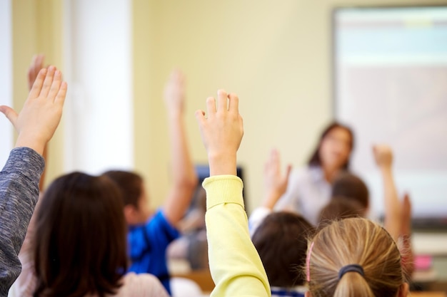 Foto concetto di istruzione, scuola elementare, apprendimento e persone - gruppo di studenti che alzano le mani durante la lezione in classe