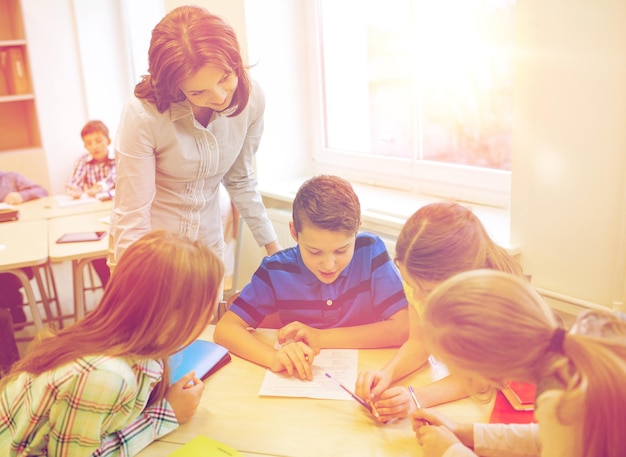 Foto istruzione, scuola elementare, apprendimento e concetto di persone - insegnante che aiuta i bambini delle scuole a scrivere il test in classe