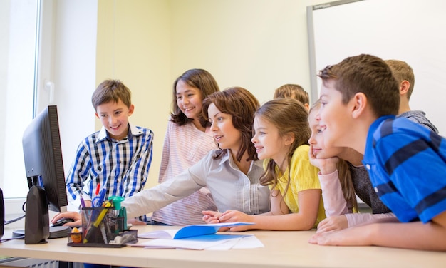 education, elementary school, learning, technology and people concept - group of school kids with teacher looking to computer monitor in classroom