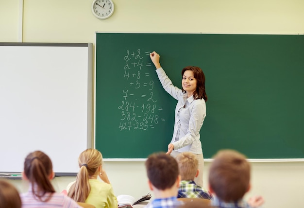 教育、初等、教育、数学、人々の概念-教室の緑の黒板に数学のタスクを書く学校の子供たちと教師のグループ