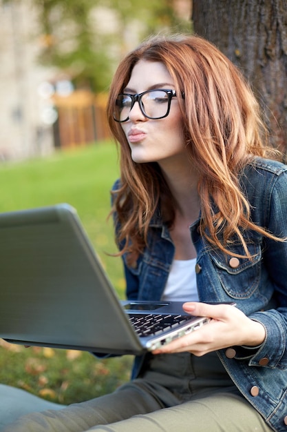 education, flirting, distant relationship, virtual communication and love concept - happy student girl with laptop computer sending air kiss at campus