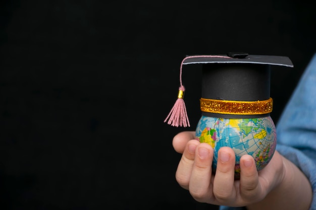 Istruzione nel mondo globale tappo di laurea sulla mano della ragazza che tiene la mappa del modello del globo terrestre con sfondo radar nelle mani concetto di studio aziendale globale all'estero educativo ritorno a scuola