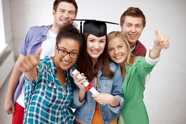 Foto concetto di educazione, laurea, gesto e persone - gruppo di studenti sorridenti in sparviere con diploma che mostra i pollici in su