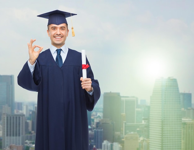 education, graduation, gesture and people concept - smiling adult student in mortarboard with diploma showing ok hand sign over city background