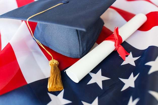 education, graduation, patriotism and nationalism concept - close up of bachelor hat and diploma on american flag