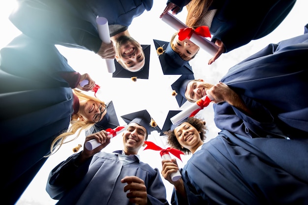 Photo education, graduation and people concept - group of happy international students in mortar boards and bachelor gowns standing in circle with diplomas