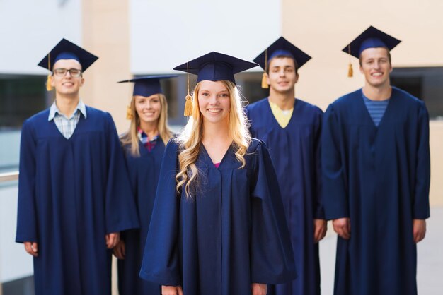 Concetto di educazione, laurea e persone - gruppo di studenti sorridenti in sparvieri e abiti all'aperto