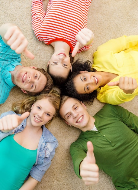 education and happiness concept - group of young smiling people lying down on floor in circle and showing thumbs up