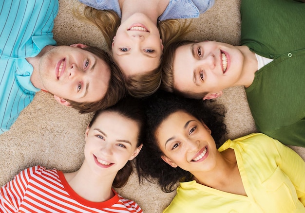 education and happiness concept - group of young smiling people lying down on floor in circle