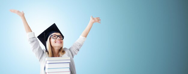 Foto concetto di educazione, felicità, laurea e persone - foto di uno studente felice in un cappello da mortaio con una pila di libri su sfondo blu