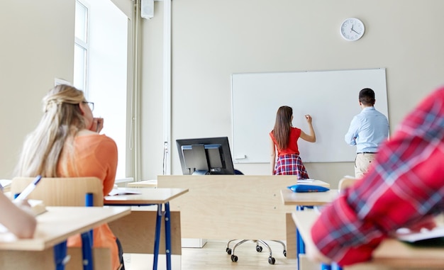 Photo education, high school, learning and people concept - student girl writing something on blank white board and teacher in classroom