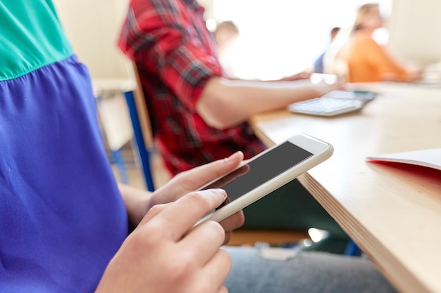 Foto educazione, scuola superiore, apprendimento, tecnologia e concetto di persone - primo piano di una studentessa con sms sullo smartphone durante la lezione