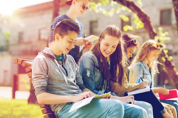 education, high school and people concept - group of happy teenage students with notebooks learning at campus yard