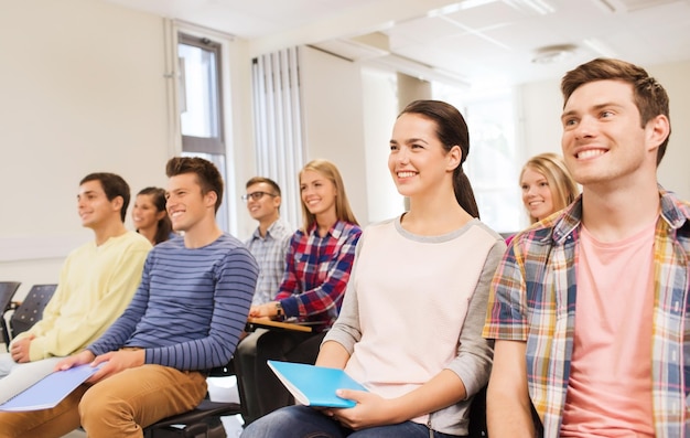 Фото Образование, средняя школа, командная работа и концепция людей - группа улыбающихся студентов с блокнотами, сидящих в лекционном зале