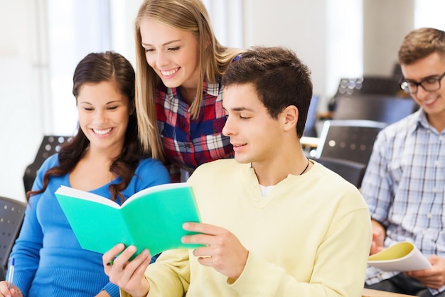 education, high school, teamwork and people concept - group of smiling students with notebook sitting in lecture hall and writing