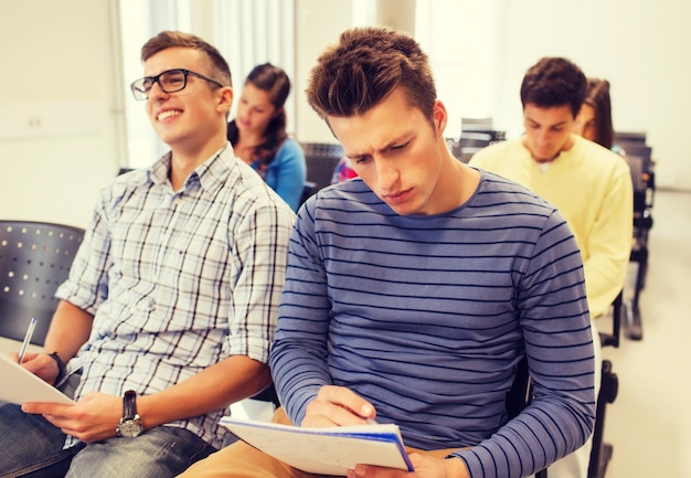 education, high school, teamwork and people concept - group of smiling students with notepads sitting in lecture hall