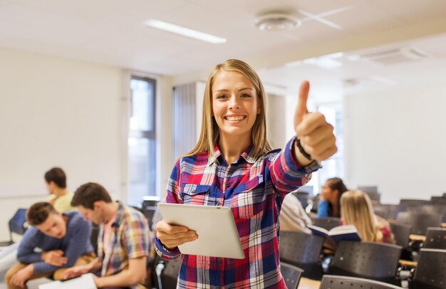 education, high school, teamwork and people concept - group of smiling students with tablet pc computer howing thumbs up in lecture hall