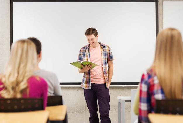 Photo education, high school, teamwork and people concept - smiling student boy with notebook standing and reading in front of students in classroom