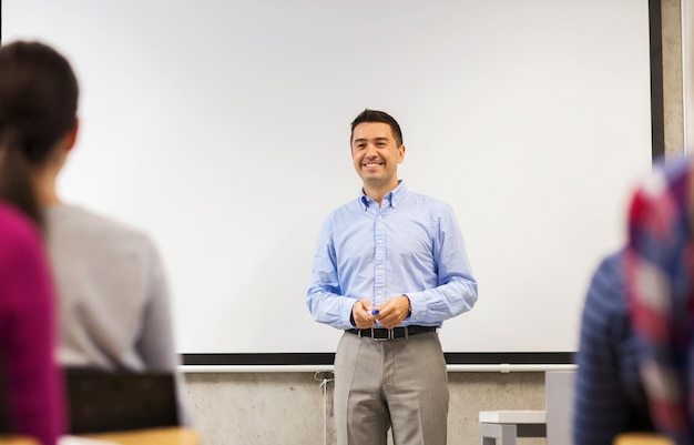 education, high school, teamwork and people concept - smiling teacher standing in front of white board and students in classroom