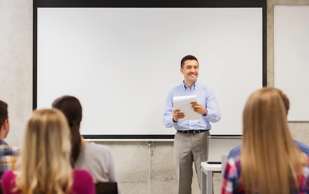 education, high school, technology and people concept - smiling teacher with notepad, laptop computer standing in front of students and showing something on white board in classroom