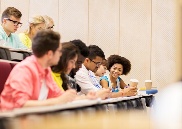 Photo education, high school, university, learning and people concept - group of international students with notebooks and coffee writing test in lecture hall