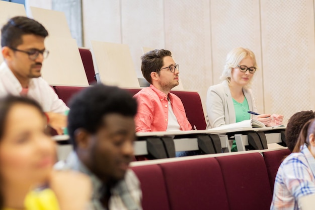Photo education, high school, university, learning and people concept - group of international students with notebooks in lecture hall and talking