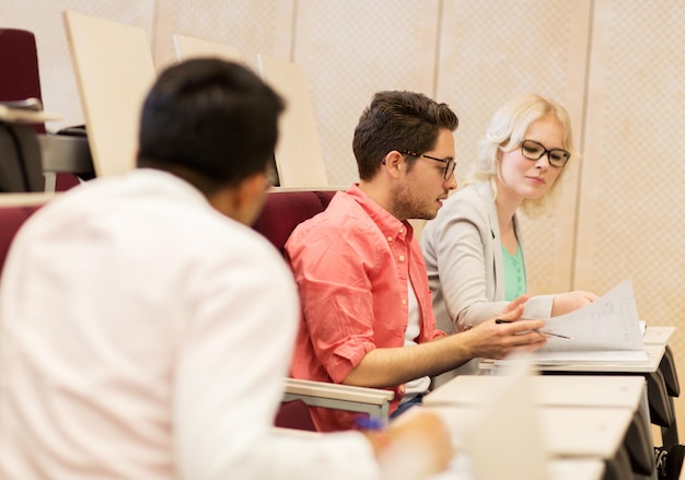 Photo education, high school, university, learning and people concept - group of international students with notebooks in lecture hall and talking