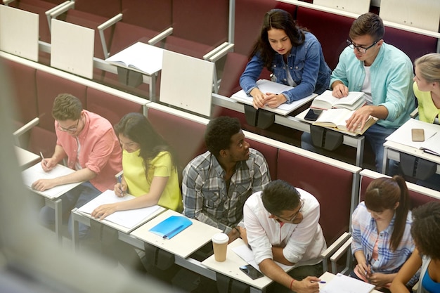 Photo education, high school, university, learning and people concept - group of international students with notebooks talking at lecture hall (shot through glass)